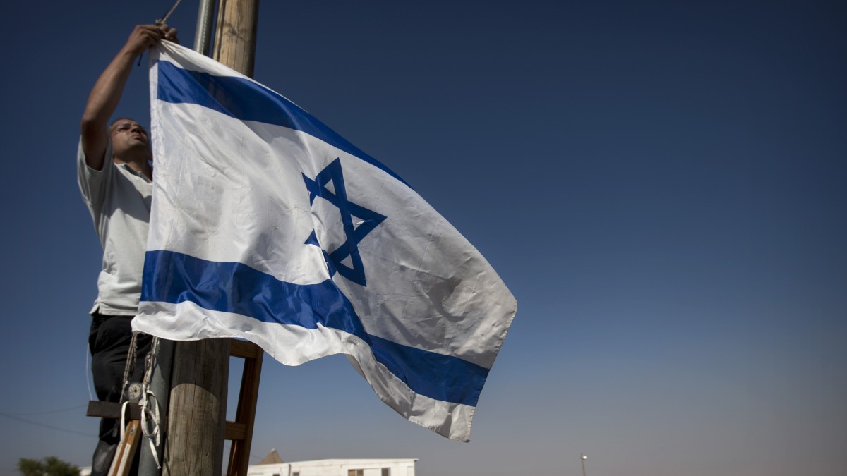 A Jewish settler hangs and Israeli flag in the unauthorized West Bank Jewish settlement of Migron. Sunday, Aug. 26, 2012. (AP Photo/Sebastian Scheiner)