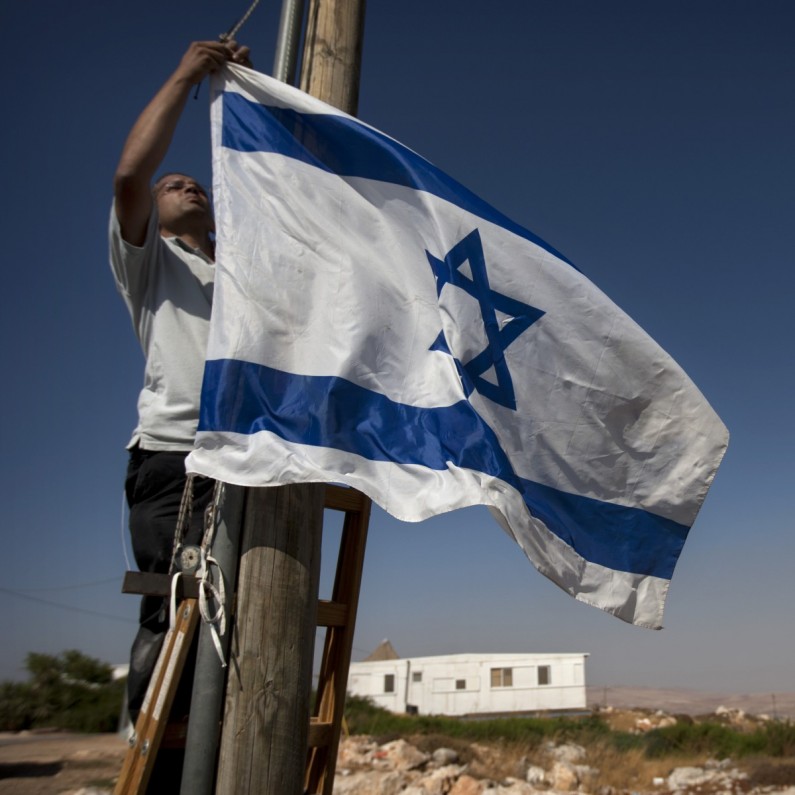 A Jewish settler hangs and Israeli flag in the unauthorized West Bank Jewish settlement of Migron. Sunday, Aug. 26, 2012. (AP Photo/Sebastian Scheiner)