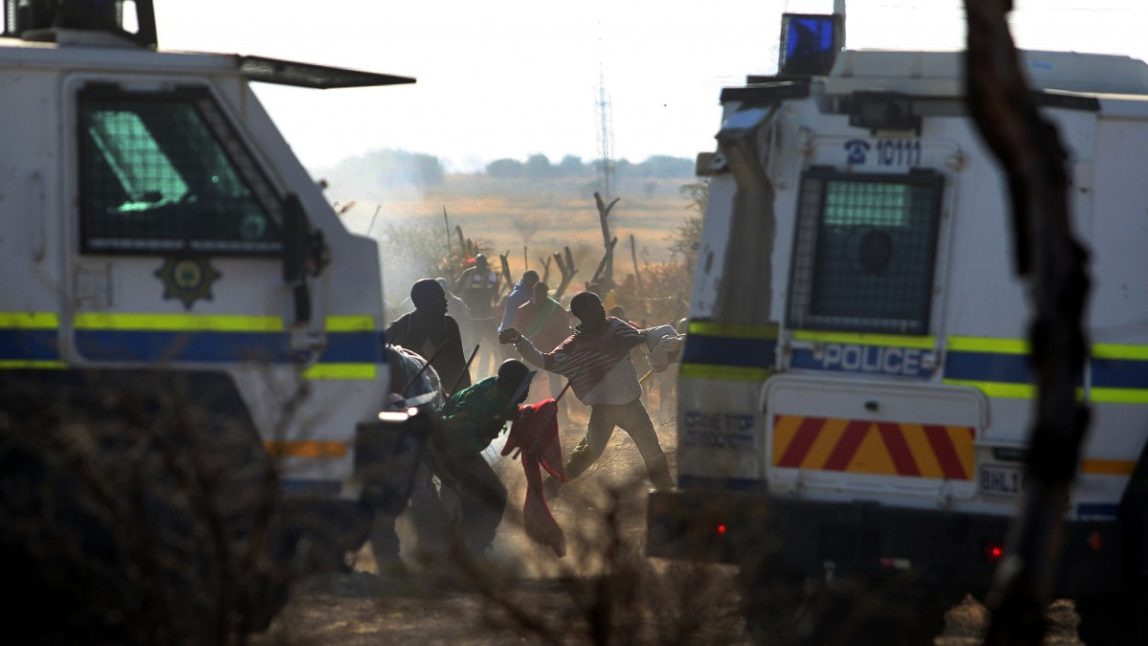 Striking mineworkers throw stones as police open fire on striking miners at the Lonmin Platinum Mine near Rustenburg, South Africa, Thursday, Aug. 16, 2012. (AP Photo)