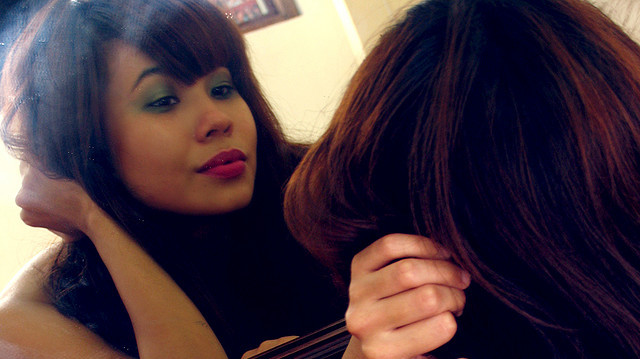 A woman looks at herself in the mirror. (Photo by Helga Weber via Flikr)