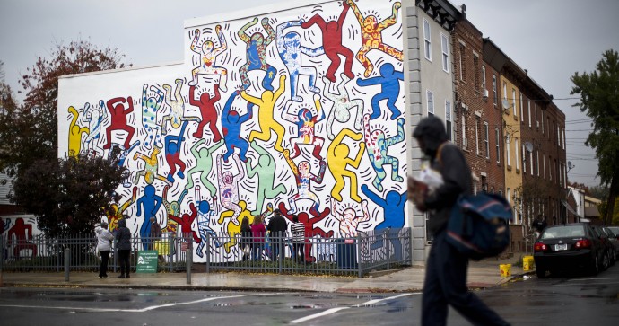 A postal worker walks past a 1987 mural titled "We The Youth" by artist Keith Haring Wednesday, Oct. 30, 2013, in the Point Breeze neighborhood of Philadelphia. The city’s Mural Arts Program has worked for months to restore the only collaborative public mural by Haring that is still intact and at its original site. Haring died of AIDS in 1990 at the age of 31. (AP Photo/Matt Rourke)