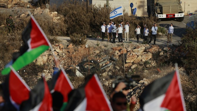 Israeli Jewish settlers hold an Israeli flag while Palestinian protesters wave Palestinian flags during a protest against the Prawer Plan to resettle Israel’s Palestinian Bedouin minority from their villages in the Negev Desert, near the Israeli settlement of Bet El, north of the West Bank city of Ramallah, Saturday, Nov. 30, 2013. (AP Photo/Majdi Mohammed)