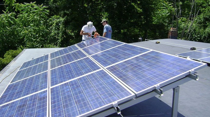 Two workers installing a tilt-up photovoltaic array on a roof near Poughkeepsie, NY. (Photo/Lucas Braun via Wikimedia Commons)