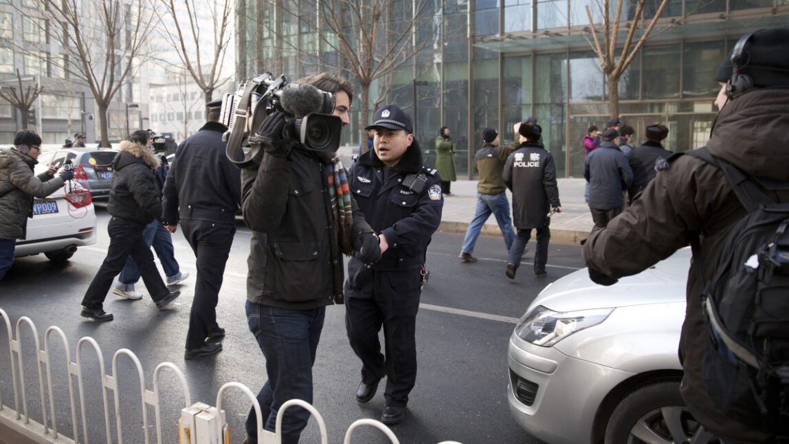 In this Sunday, Jan. 26, 2014 photo, policemen try to block journalists from interviewing Xu Zhiyong's lawyer Zhang Qingfang as he speaks to the media near the No. 1 Intermediate People's Court, in Beijing. The government is intensifying efforts to control foreign media coverage of China, blocking websites, harassing reporters trying to cover trials of activists in Beijing and thwarting efforts by The New York Times to station new journalists on the mainland. (AP Photo/Andy Wong)