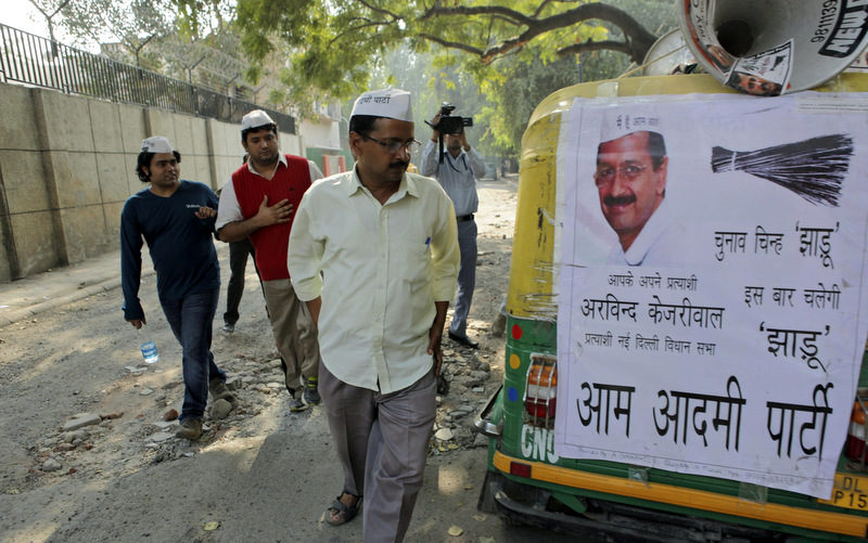 Arvind Kejriwal, center, leader of the Aam Aadmi Party, or the Common Man's Party, looks at an auto rickshaw displaying a poster in support of his party, ahead of the Delhi state assembly elections in New Delhi, India. Election season in India always comes with heaps of promises, as political parties try to woo voters with everything from subsidized fuel and electricity to free laptops, spice grinders, even goats and cows. But there are growing concerns that freebies will hurt the country's sputtering economy. (AP Photo/Tsering Topgyal, FIle)