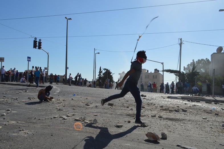 Young man from Shufat launches stones towards IDF with a catapult, while other residents keep out of army fire.(Photo by Matthew Vickery for Mint Press)