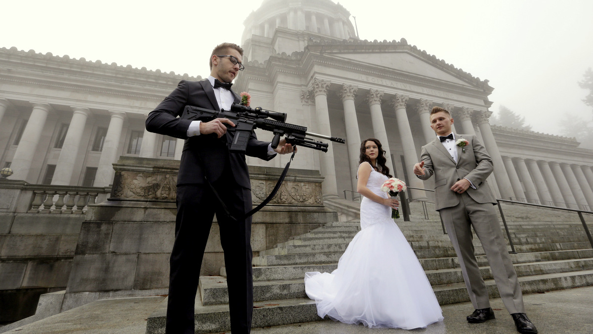 The best man in a wedding party, who all declined to be identified, holds an AR-10 rifle he was handed while the party was having their pre-wedding portraits taken on the steps of the capitol before a rally nearby by gun-rights advocates to protest a new expanded gun background check law in Washington state 