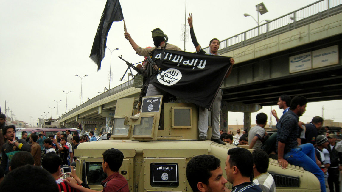 Islamic State group militants hold up their flag as they patrol in a commandeered American in Fallujah, 40 miles (65 kilometers) west of Baghdad, Iraq. (AP Photo)