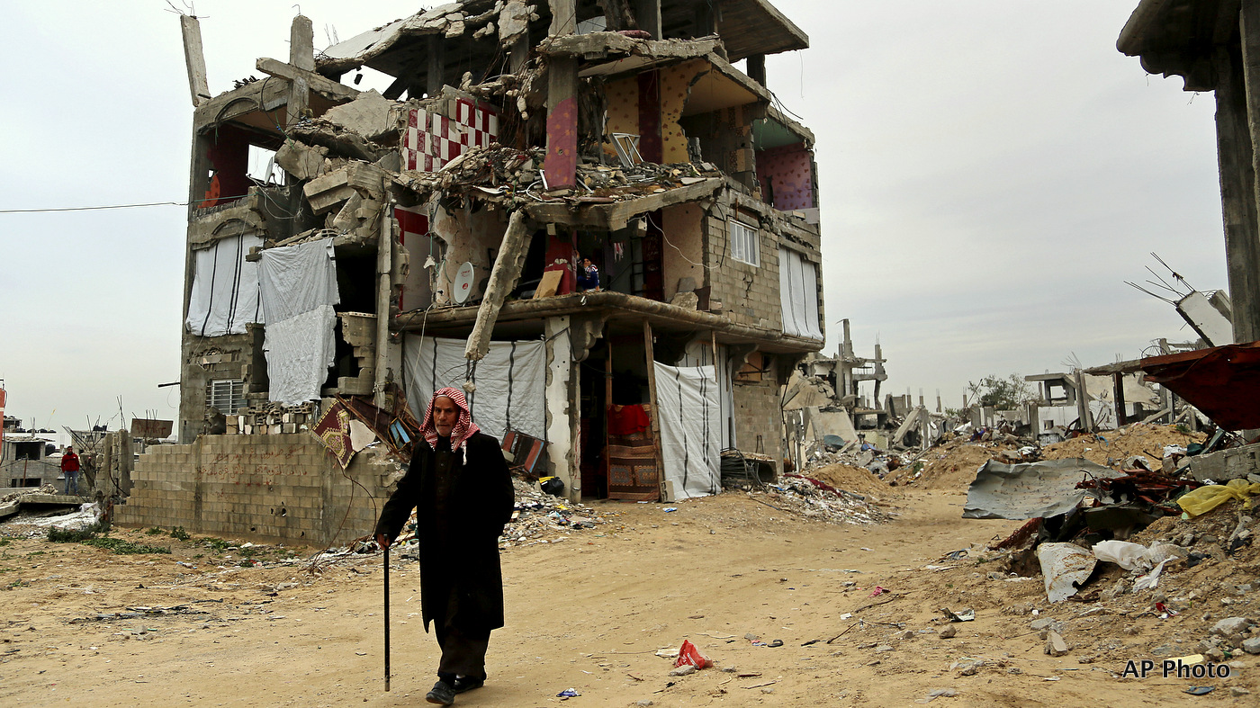 A elderly Palestinian walks past a building which was damaged in last summer's war, in the Shijaiyah neighborhood of Gaza City, northern Gaza Strip, Monday, Feb. 23, 2015. 