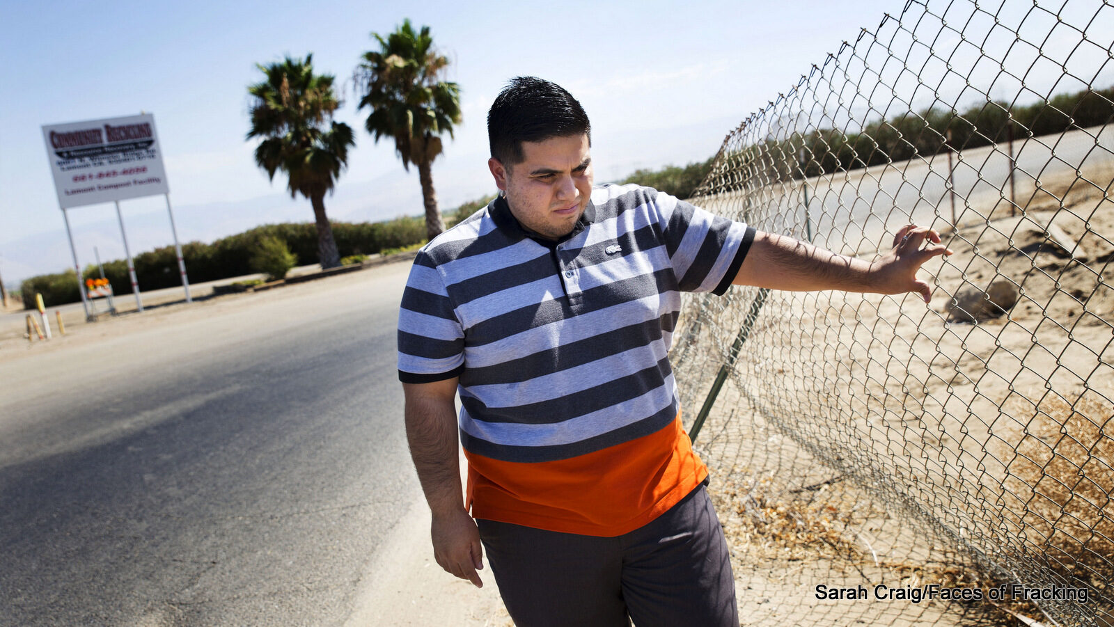 Gustavo Aguirre Jr. stands in front of a noxious "recycling" facility where he and his team takes air samples. A shrine in front of the entrance commemorates two brothers who died of hydrogen sulfide poisoning while working there; a reminder of the dangers of living and working in near fracking facilities.