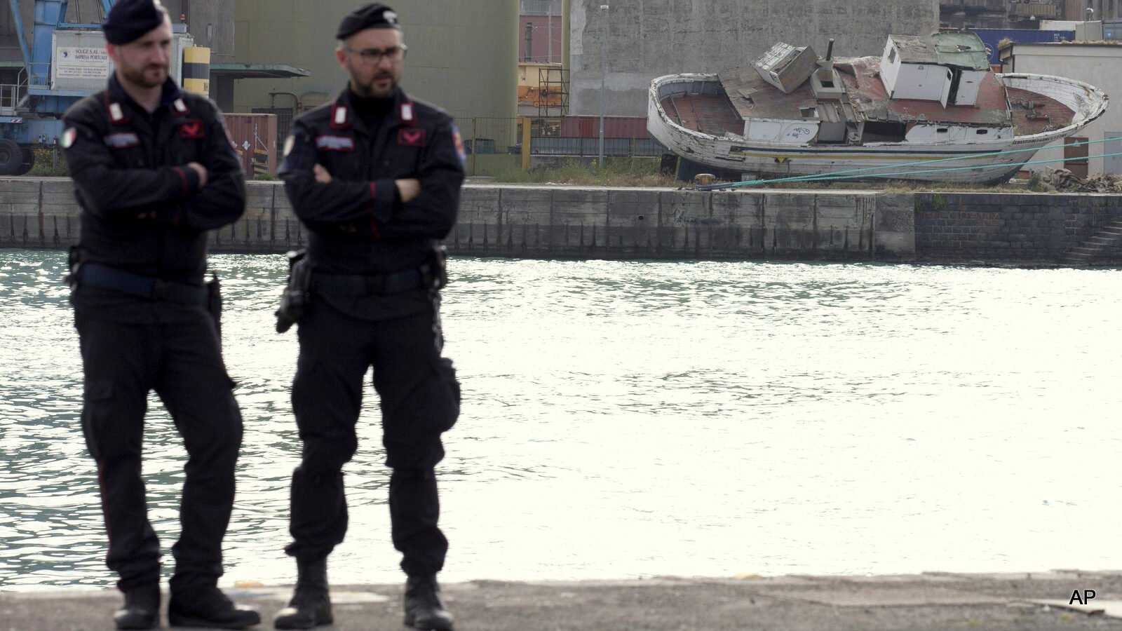 Italian forces stand guard in front of the wreckage of a boat used by migrants in Catania's Harbour, Italy, Monday, April 20, 2015.