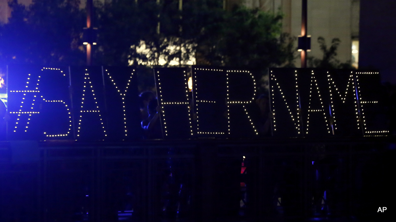Protestors hold up a lighted sign reading "#say her name" during a vigil for Sandra Bland