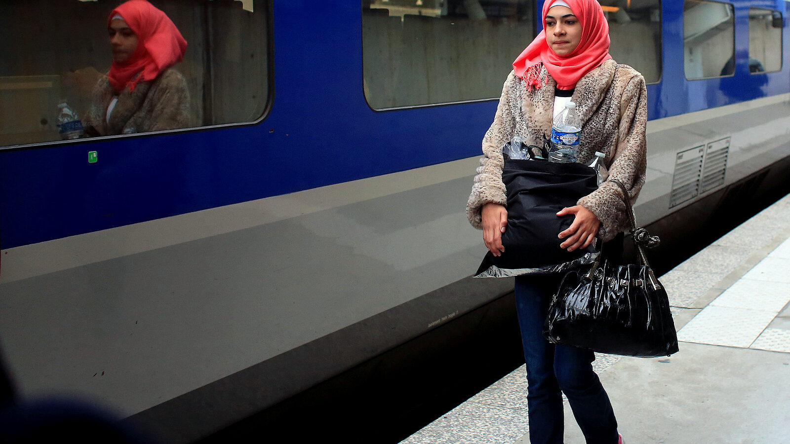 Syrian refugee Isra Abomosa, 18, carries belongings before boarding a train to Vannes, western France, in the Montparnasse railway station, in Paris, France .Her slain husband, bombed-out Damascus home and refugee life are behind her. (AP Photo/Thibault Camus)