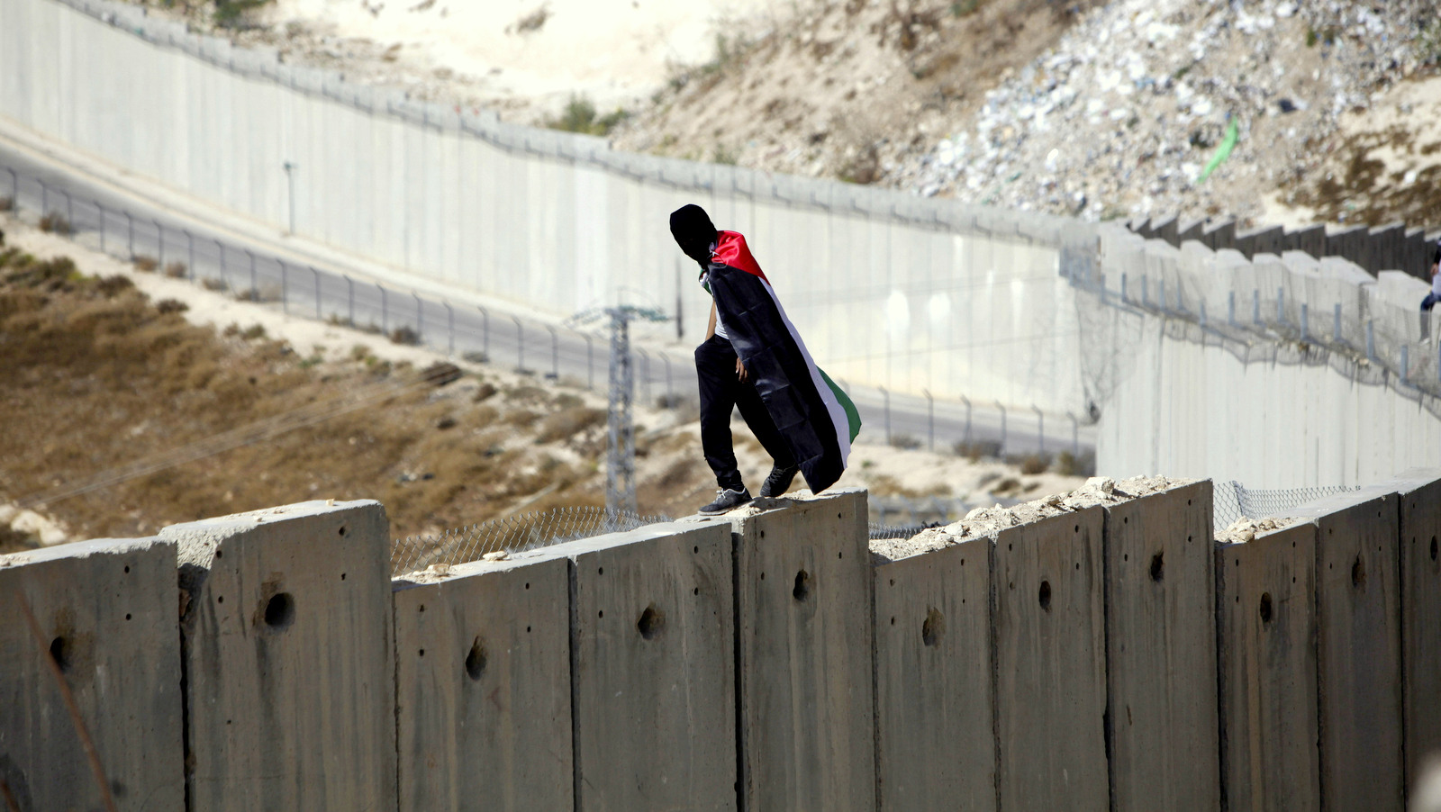 在2015年11月2日星期一的抗议活动期间，一名身穿巴勒斯坦国旗的学生走过以色列在阿布迪斯的西岸和以色列之间的种族隔离墙。（美联社照片/ Mahmoud Illean）