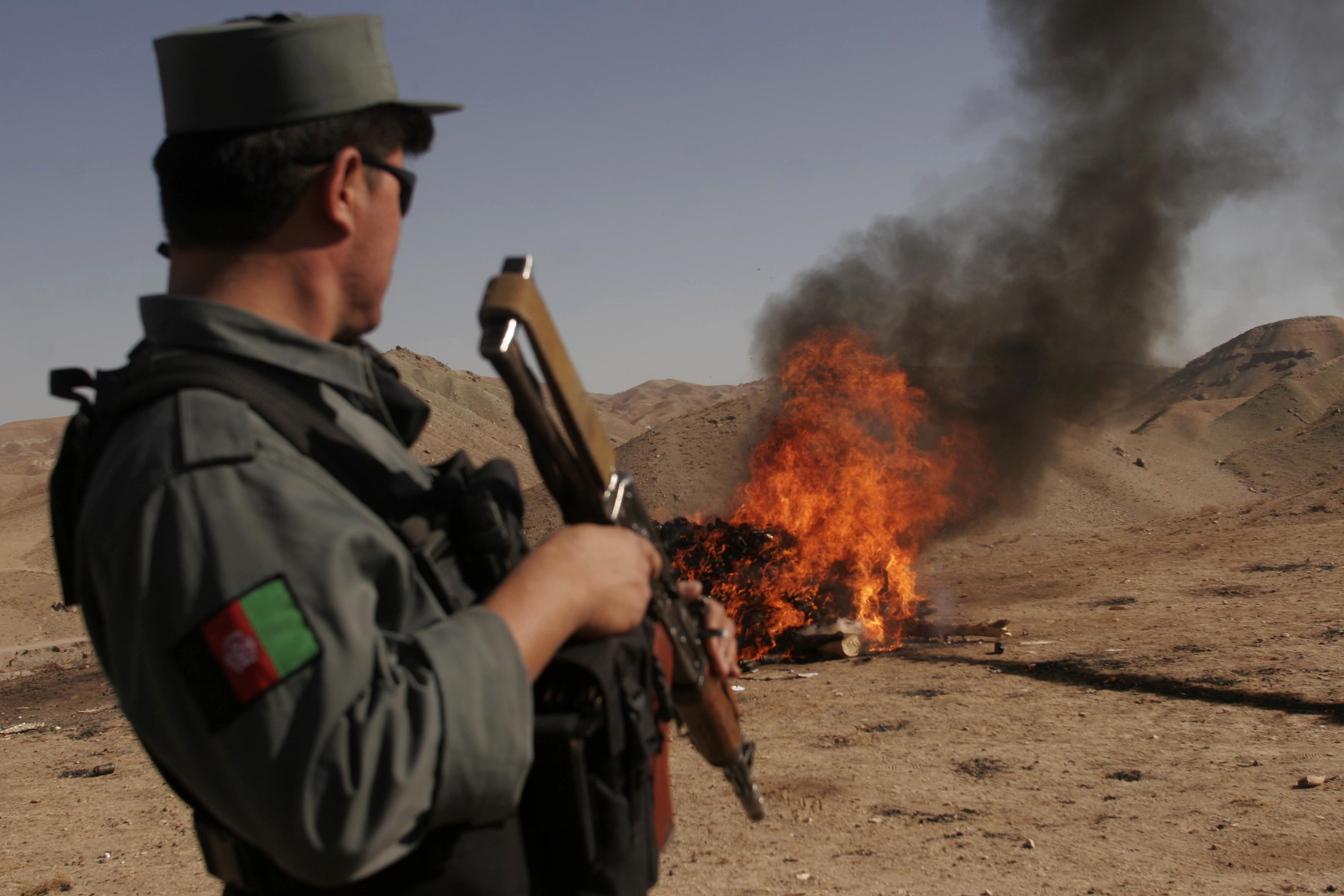 An Afghan security policeman stands guard as the smoke rises from a fire of confiscated drugs and alcohol on the outskirts of the city in Herat, south west of Kabul, Afghanistan on Nov, 11, 2007. (AP/Fraidoon Pooyaa)