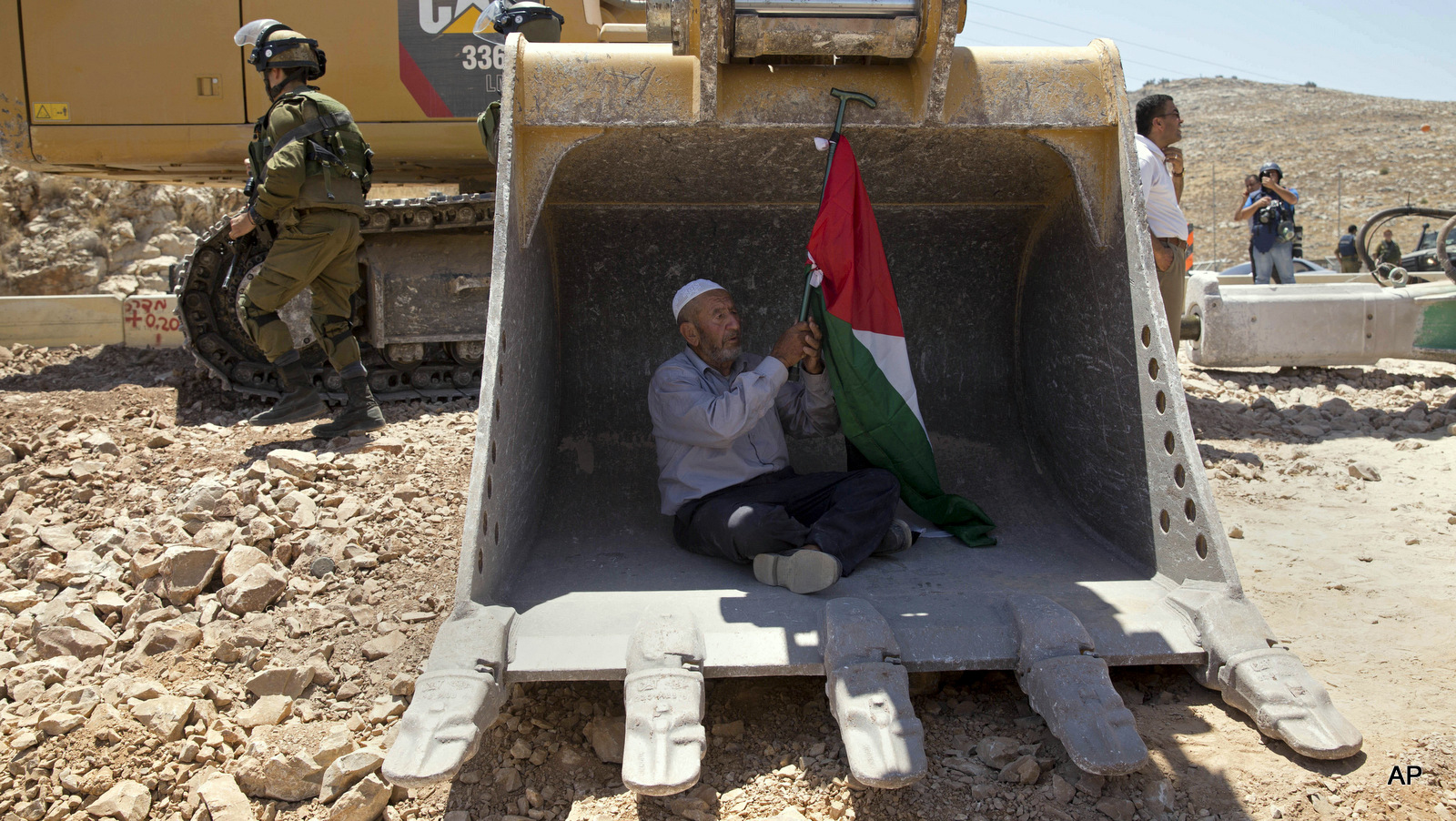 A Palestinian man tries to stop work by an Israeli bulldozer during a protest outside the village of Deir Qaddis, near the West Bank city of Ramallah, Wednesday, July 13, 2016. Dozens of Palestinians demonstrated Wednesday in front of Israeli bulldozers that were bulldozing land outside Deir Qaddis village near Ramallah for an apparent plan to expand a nearby Jewish settlement. The protesters forced the bulldozers to stop, but residents said they resumed work after the protesters left the area.