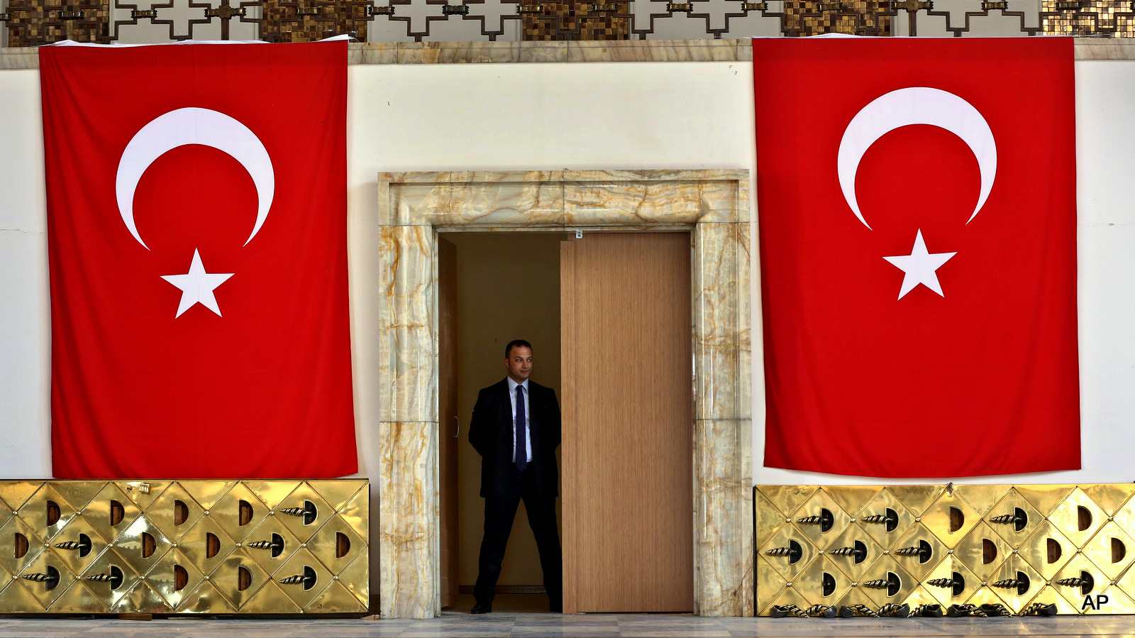 A Turkish parliament security man stands guard next to the broken yellow copper doors laid on the ground at the entrance of the assembly hall at the parliament building which was attacked by the Turkish warplanes during the failed military coup last Friday, in Ankara, Turkey, Tuesday, July 19, 2016.
