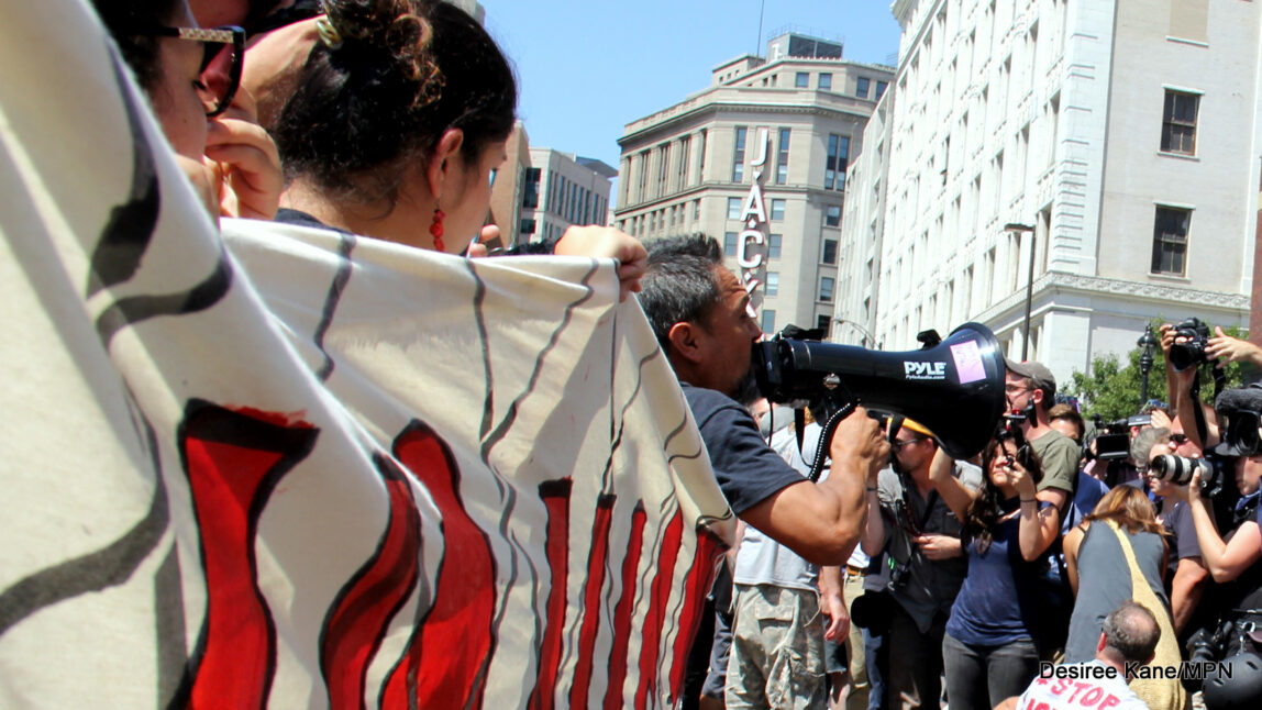July 19, 2016. As activists build a mock wall in front of the Republican National Convention, others protect them with joined hands, while media films their action.