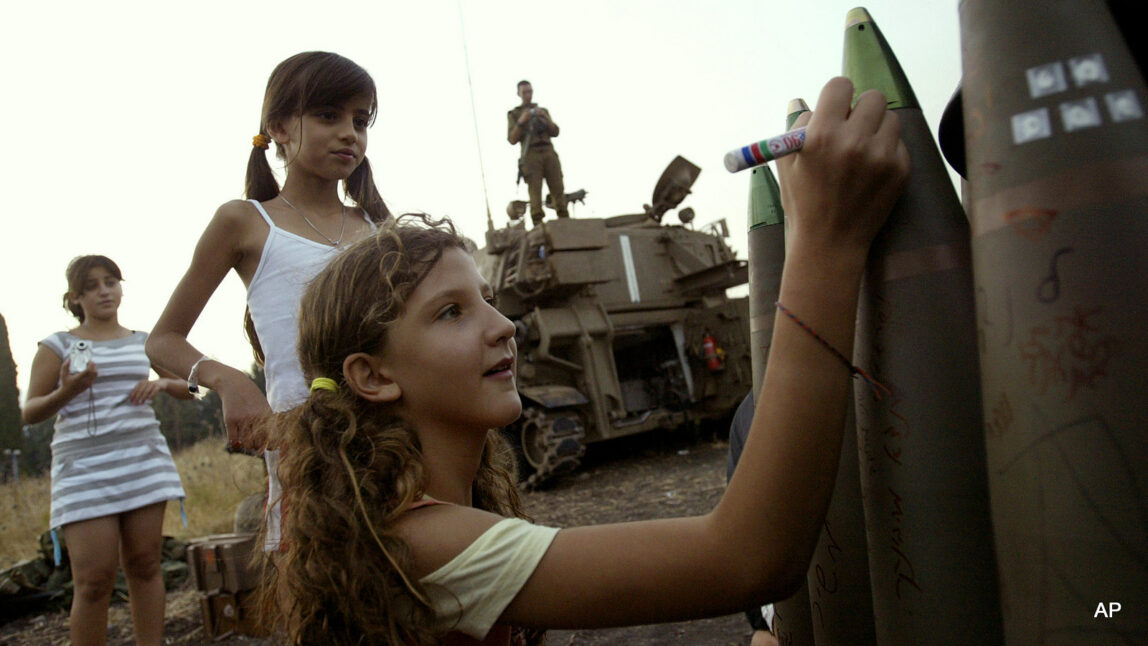 Israeli girls write messages on a bombs at a heavy artillery position near Kiryat Shmona, in northern Israel, next to the Lebanese border, Monday, July 17, 2006. (AP Photo/Sebastian Scheiner)