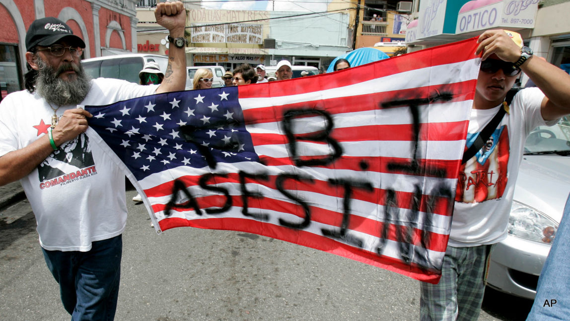 Pro-independence activists march holding a U.S. flag with a graffiti that reads: "FBI killers" in the town of Lares, Puerto Rico.
