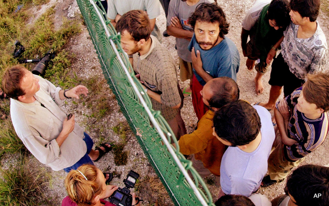 In this Sept. 19, 2001, file photo, refugees, right, gather on one side of a fence to talk with international journalists about their journey that brought them to the Island of Nauru. Human rights groups accused Australia on Wednesday, Aug. 3, 2016, of deliberately ignoring the abuse of asylum seekers being held at the remote Pacific island detention camp in a bid to deter future refugees from trying to reach the country by boat.