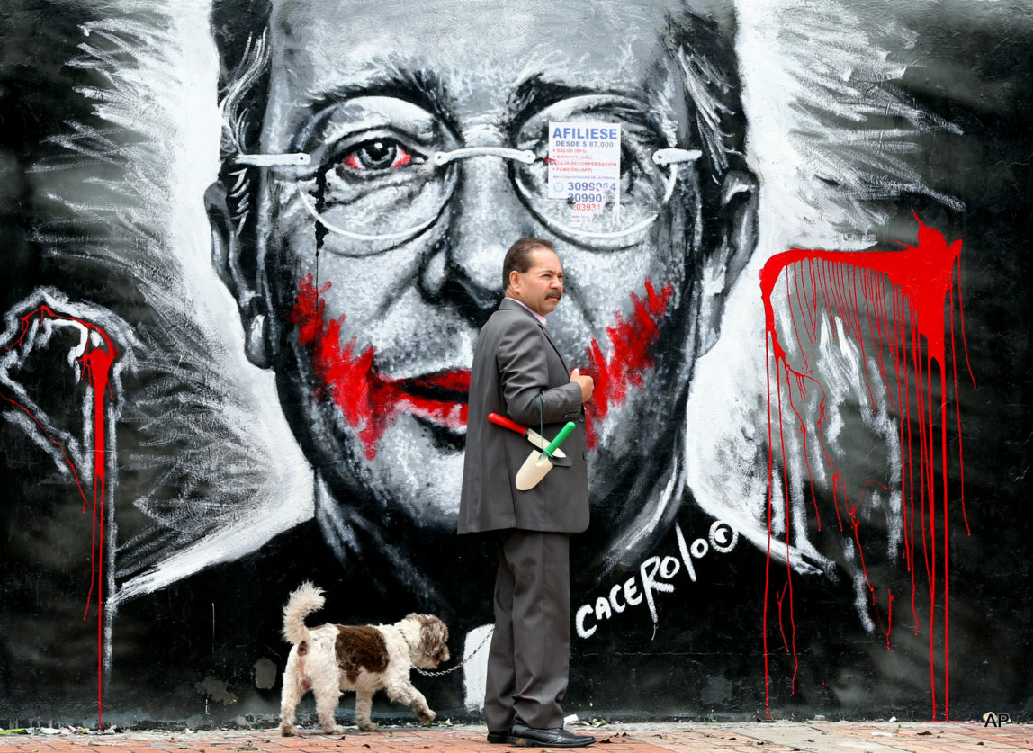 In this March 18, 2015 photo, a man walks his dog next to a mural depicting former President Alvaro Uribe, in Bogota, Colombia.