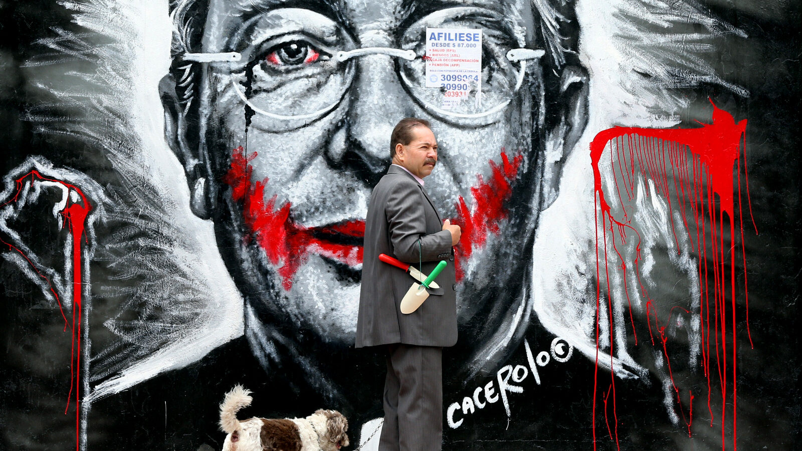 In this March 18, 2015 photo, a man walks his dog next to a mural depicting former President Alvaro Uribe, in Bogota, Colombia.