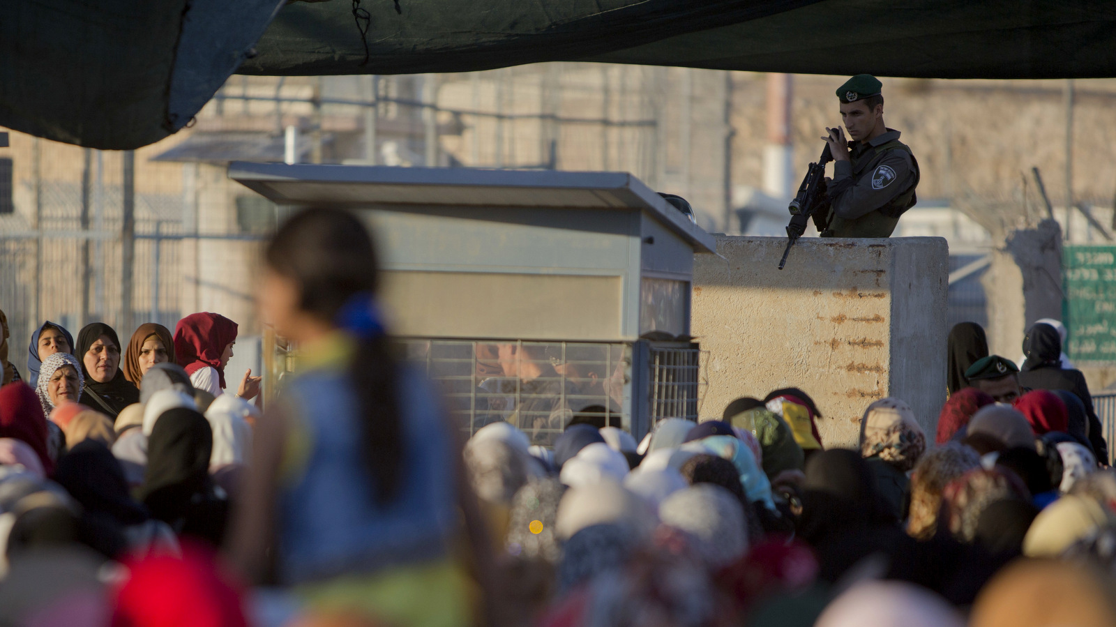 2015年6月17日，一名以色列边防警察站在巴勒斯坦妇女等待穿越约旦河西岸城市拉马拉和耶路撒冷之间的Qalandia检查站。（美联社照片/ Majdi Mohammed）