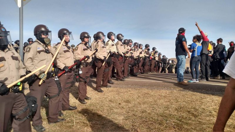 Water protectors face off with a police line off North Dakota Highway 1806. Law enforcement wear riot gear as they prepare to remove the frontline camp. Oct. 27, 2016 (Derrick Broze for MintPress) 