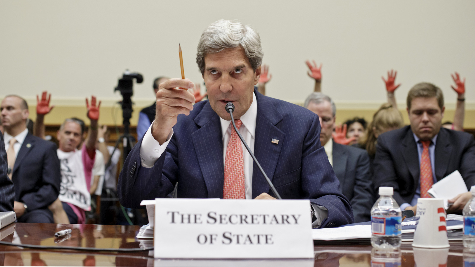 Protestors holding up their red painted hands, stand behind Secretary of State John Kerry as he testifies on Capitol Hill in Washington, Wednesday, Sept. 4, 2013, before the House Foreign Affairs Committee hearing to advance President Barack Obama's request for congressional authorization for military intervention in Syria, a response to an alleged sarin gas attack in the Syrian civil war. (AP Photo/J. Scott Applewhite)