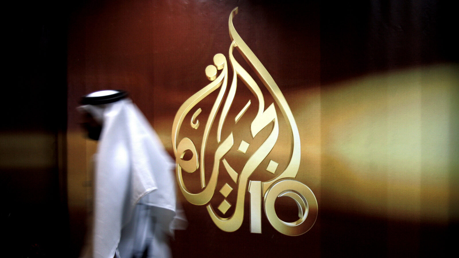 A Qatari employee of Al Jazeera Arabic language TV news channel walks past the logo of Al Jazeera in Doha, Qatar. (AP/Kamran Jebreili)