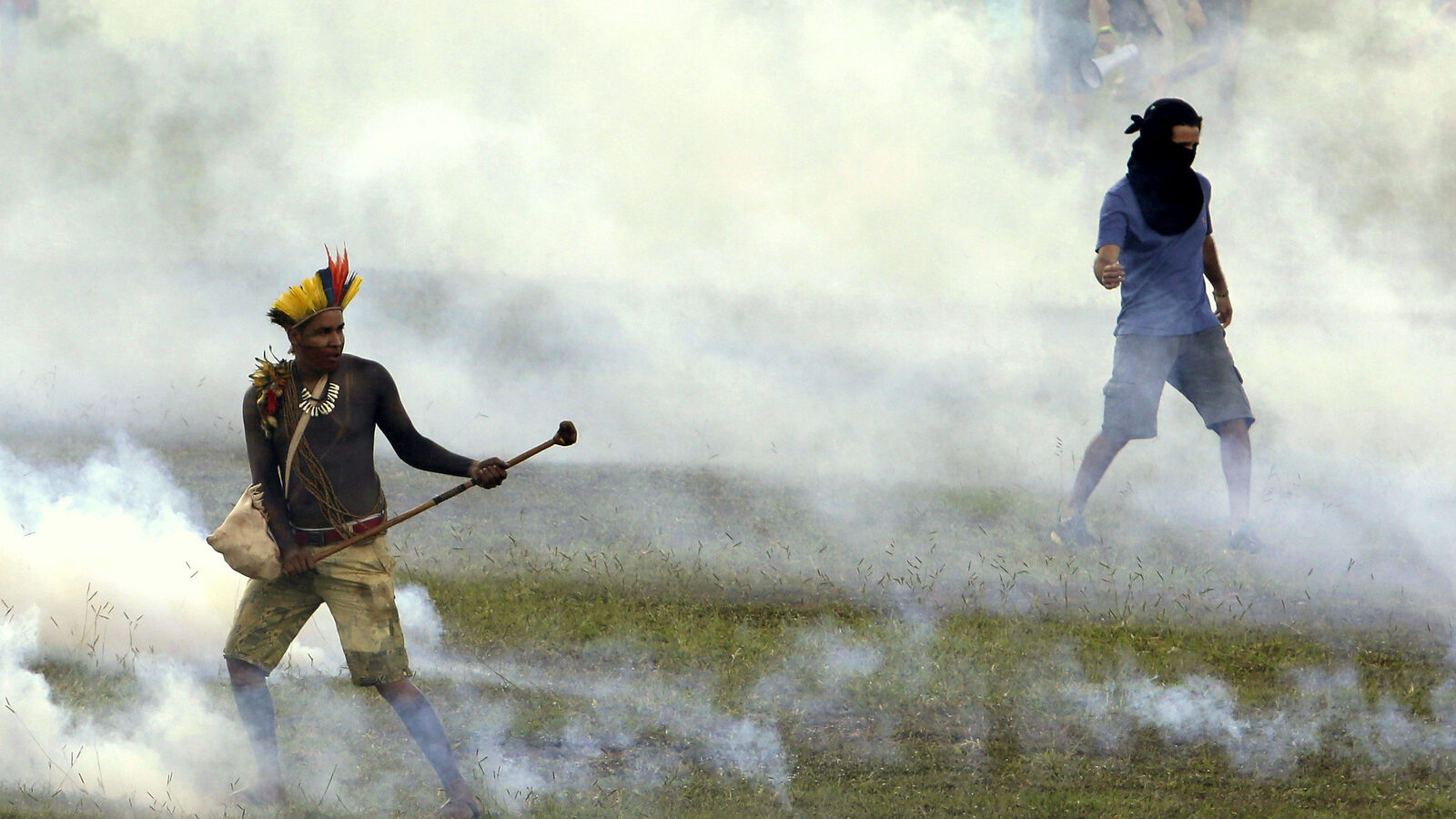 An indigenous man, left, stands amid tear gas fired by police outside the National Congress during a demonstration for the demarcation of indigenous lands in Brasilia, Brazil, Tuesday, April 25, 2017. Indigenous leaders say the government of President Michel Temer is working to roll back protections in various parts of the Amazon and allowing ranchers and other big-money interest to steal their lands. (AP/Eraldo Peres)
