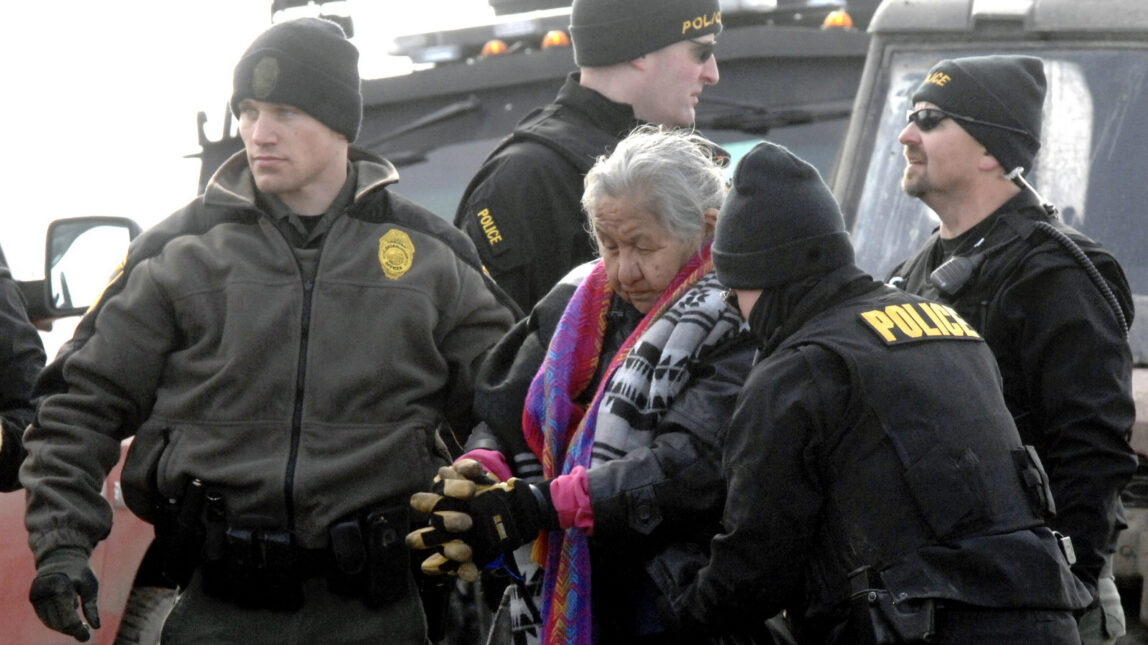 An elderly Native American woman is escorted to a transport van after being arrested by law enforcement at the Oceti Sakowin camp as part of the final sweep of the Dakota Access pipeline protesters in Morton County, Feb. 23, 2017, near Cannon Ball, N.D. (Mike McCleary/The Bismarck Tribune)