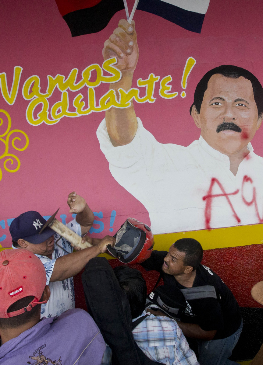 A farmer opposed to the transoceanic canal project hits a government supporter over the head with a galvanized pipe mortar, backdropped by a wall that depicts a likeness of President Daniel Ortega with the message, "Let's move forward!" in Juigalpa, Nicaragua, June 13, 2015. (AP/Esteban Felix)