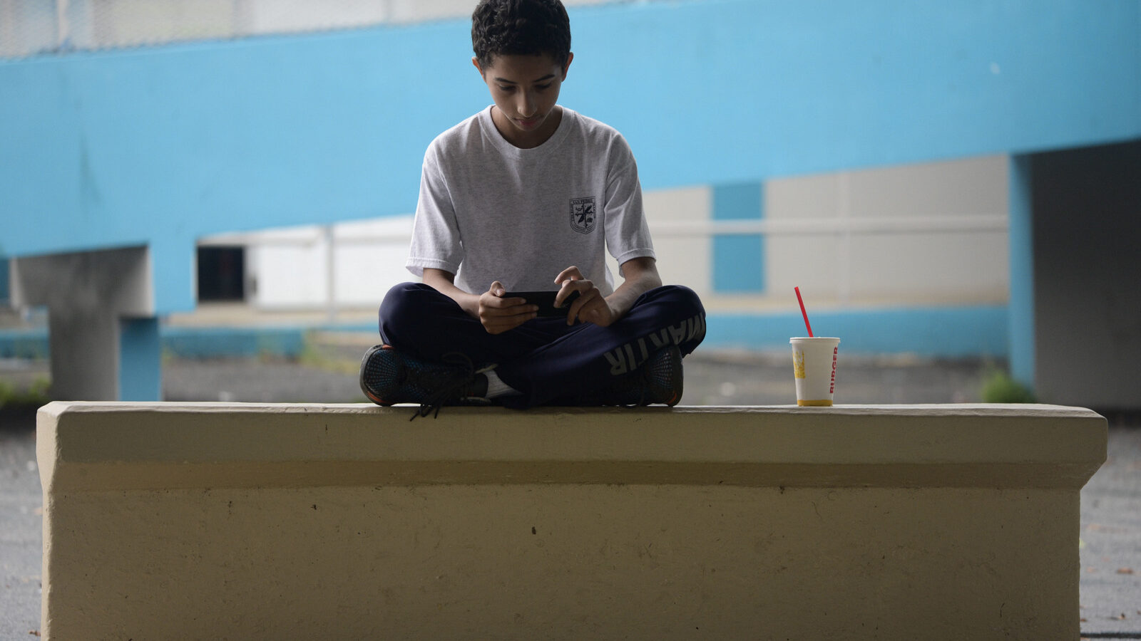 In this Friday, Oct. 13, 2017 photo, a youth sits in the courtyard of Ramon Marin Sola Elementary School, which opened its doors as a daytime community center after the passing of Hurricane Maria in Guaynabo, Puerto Rico, Most schools remain closed, leaving kids to pass the time playing on downed trees or using precious phone battery on video games, waiting for life to return to normal as the adults around them struggle to put their own lives back together. (AP Photo/Carlos Giusti)