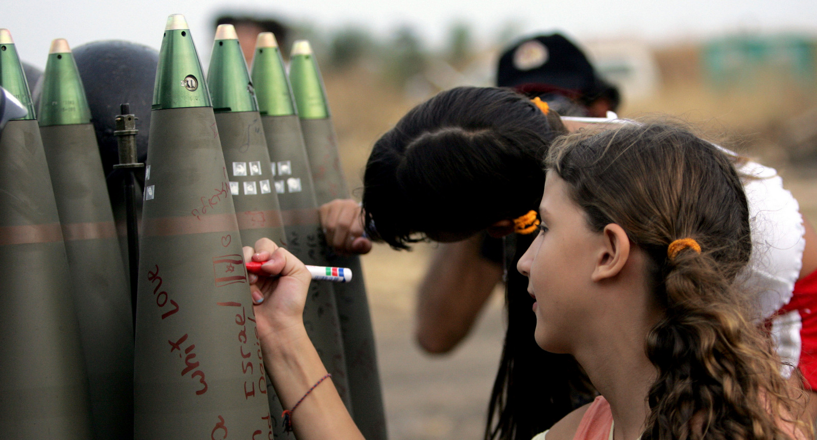 Israeli girls write messages in Hebrew on shells ready to be fire by mobile artillery unit into southern Lebanon 17 July 2006, at a military staging area along the northern Israeli border.