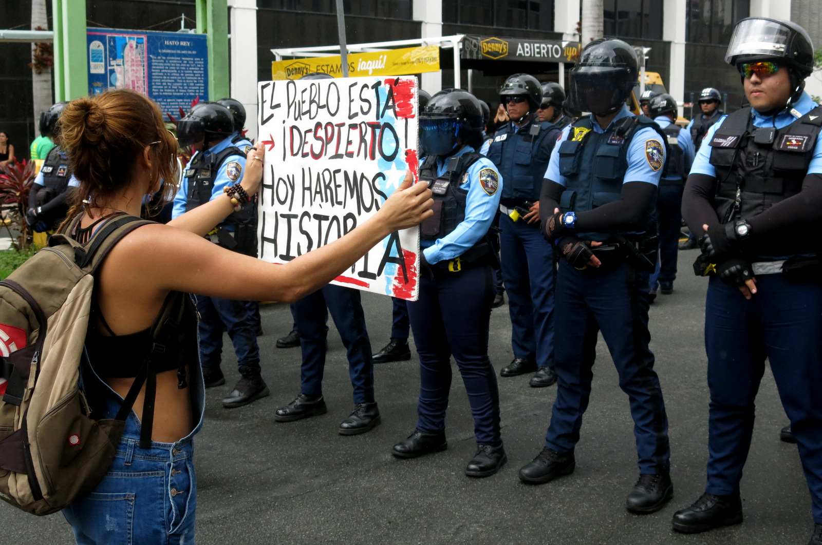 A woman holds a sign up to police that reads in Spanish "The people are awake. Today we'll make history" during a May Day protest against looming austerity measures amid an economic crisis and demanding an audit on the island's debt to identify those responsible in San Juan, Puerto Rico, May 1, 2017. Puerto Rico is preparing to cut public employee benefits, increase tax revenue, hike water rates and privatize government operations, among other things. (AP/Danica Coto)