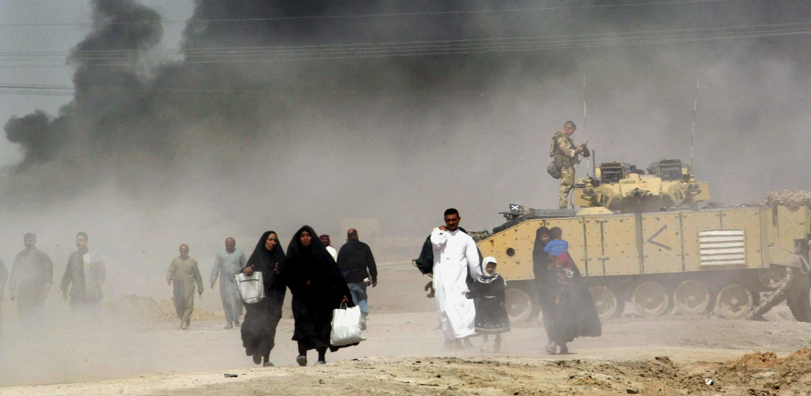 伊拉克人逃离伊拉克南部的巴士拉途中经过一辆英国坦克，2003年3月29日在远处可以看到烟雾笼罩着这座城市。（美联社/ Anja Niedringhaus）