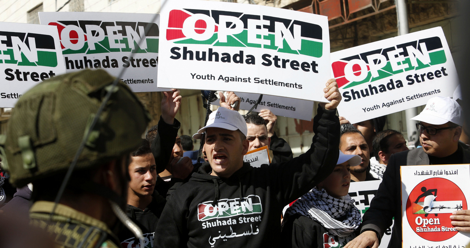 Protesters hold posters demanding the reopening of Shuhada Street in Hebron, Friday, Feb. 27, 2015. Israel closed Shuhada Street for Palestinians in 1994 after an Israeli killed 29 Palestinians and wounded over a 100 praying in a mosque. (AP/Nasser Shiyoukhi)