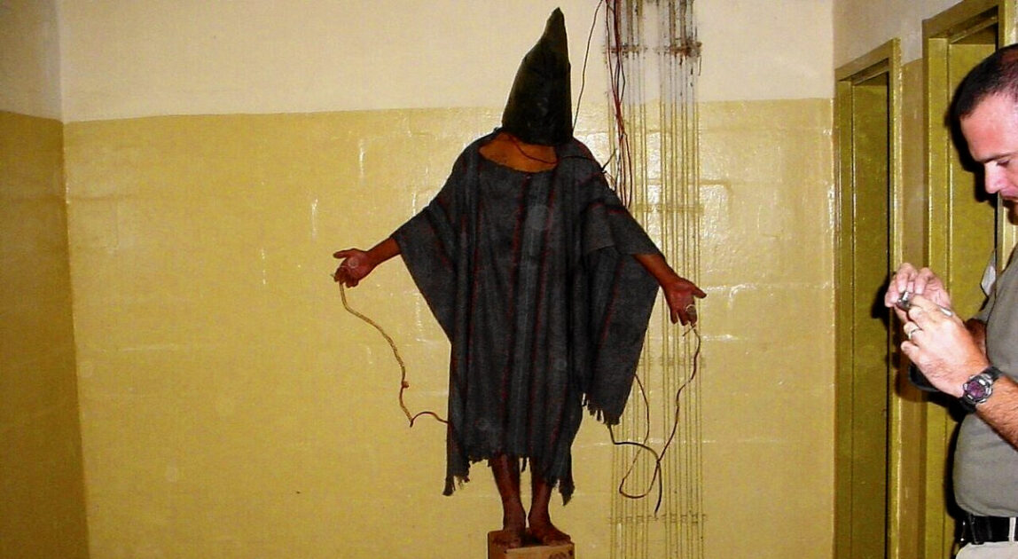 An unidentified detainee standing on a box with a bag on his head and wires attached to him in late 2003 at the Abu Ghraib prison in Baghdad, Iraq.