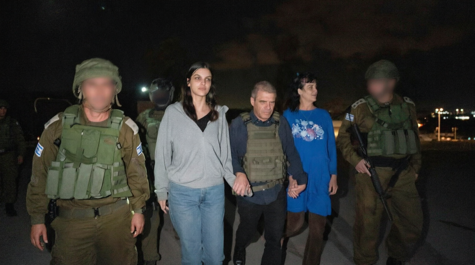 Released hostages walking with Israeli military personnel at night, faces of soldiers blurred